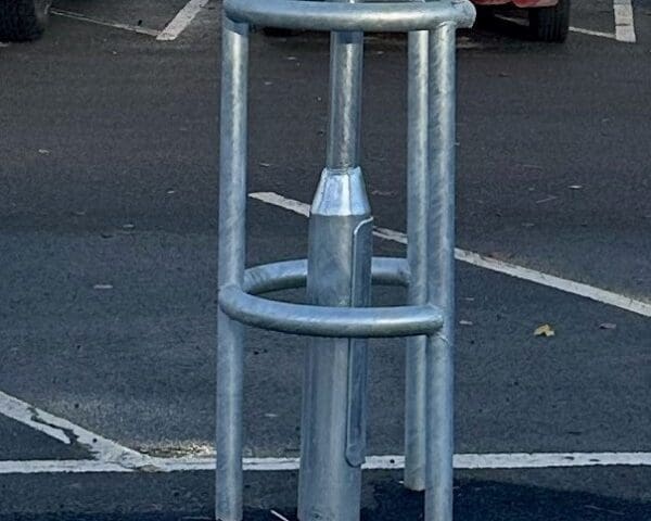 A horseshoe-shaped column protector is installed around a lamppost in a parking lot.